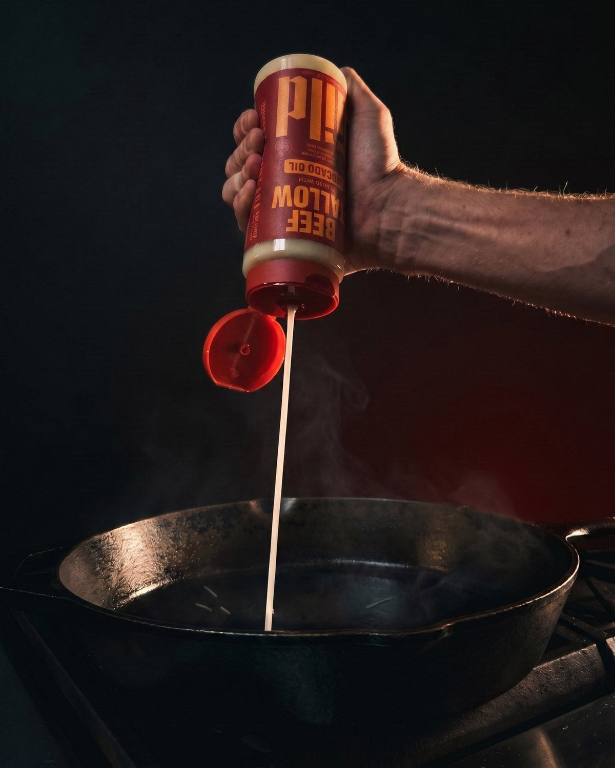 A hand squeezing GILD Beef Tallow into a hot cast-iron skillet, steam rising