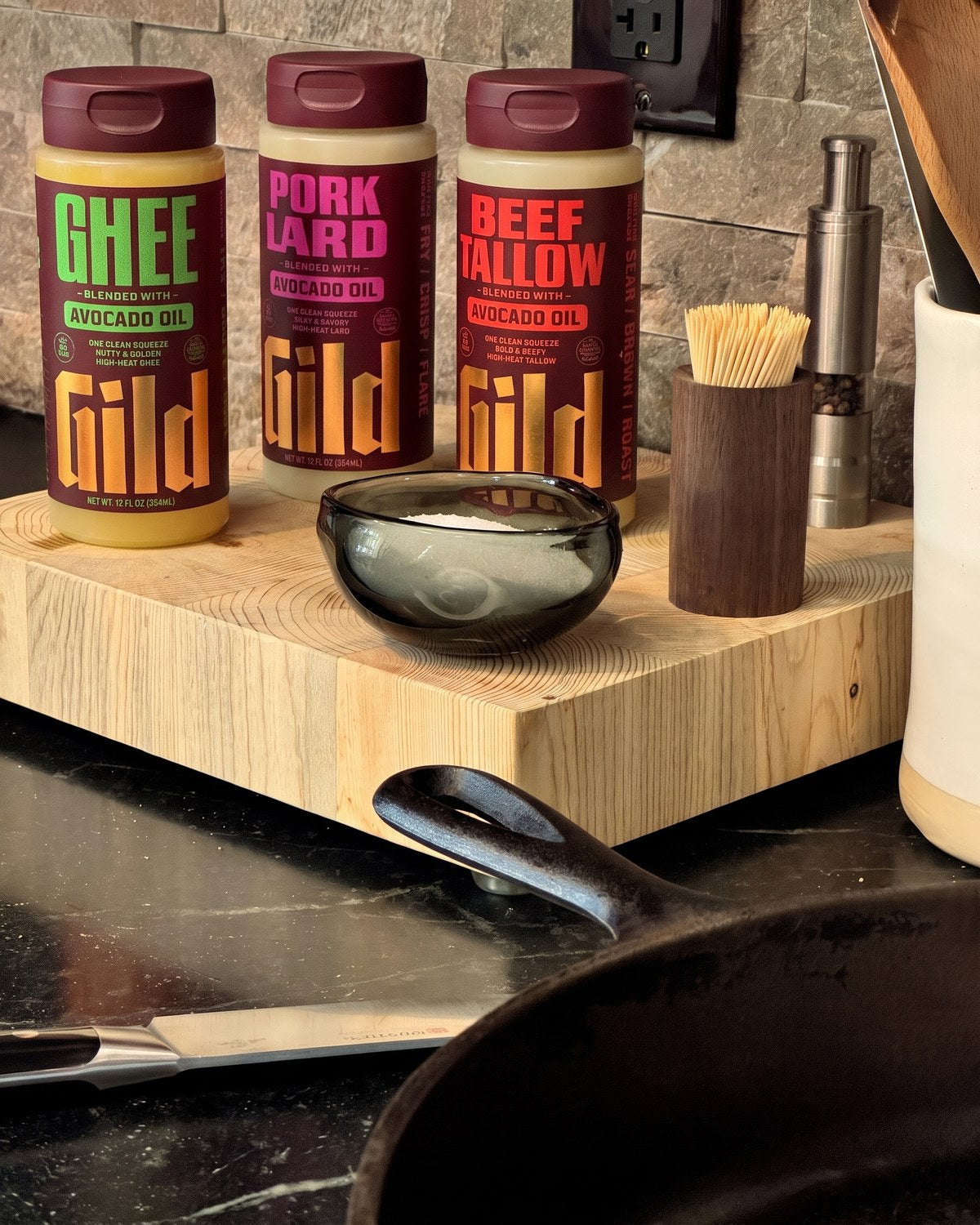 GILD Ghee, Pork Lard, and Beef Tallow on a butcher block by the stove, cast iron at the ready