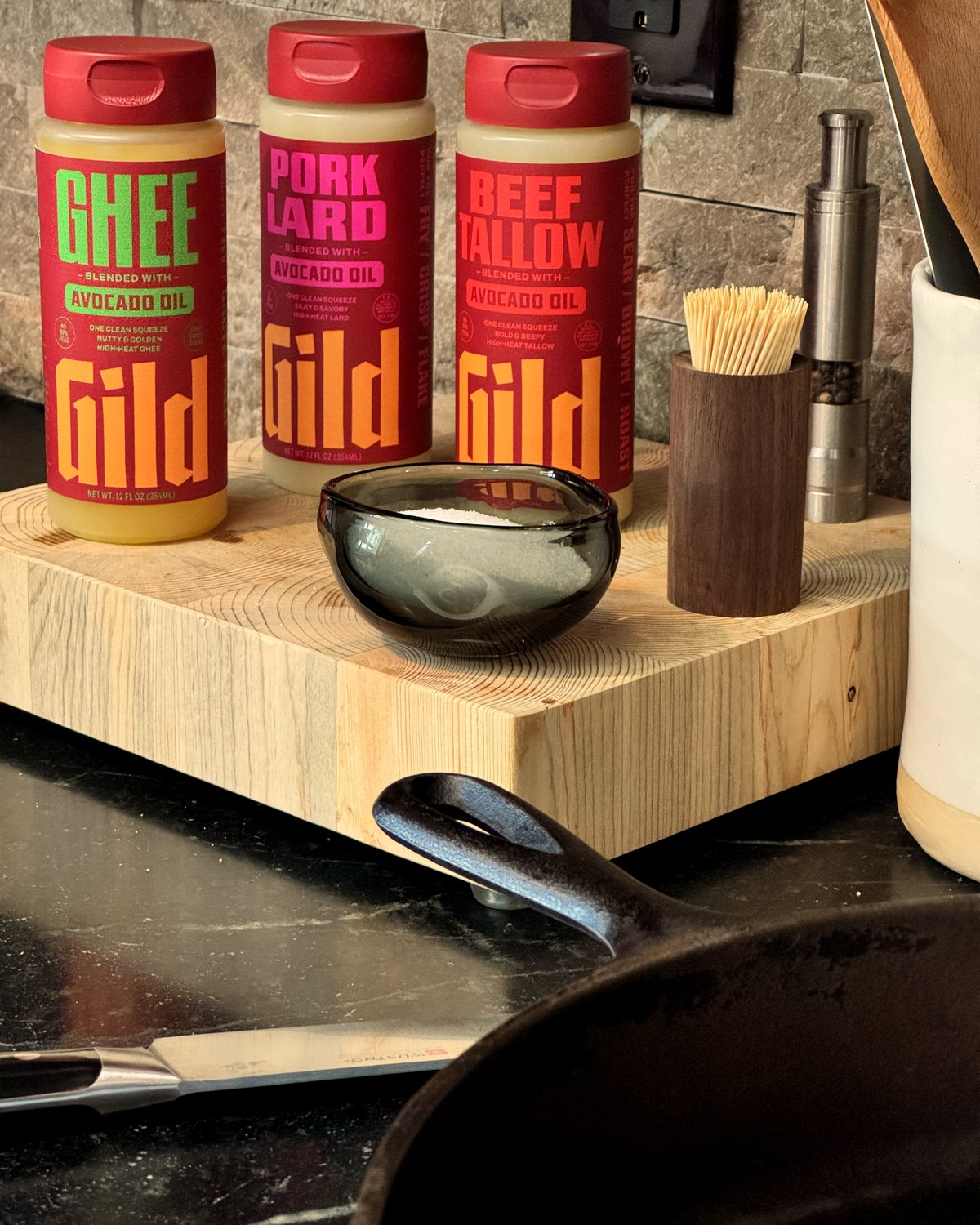 GILD Ghee, Pork Lard, and Beef Tallow on a butcher block by the stove, cast iron at the ready